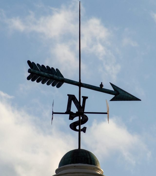 Close-up of a weather vane on a rooftop with a blue sky background