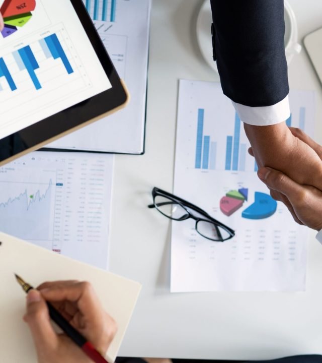 Business professionals handshake over graphs and charts in a corporate setting, symbolizing successful negotiation and agreement.