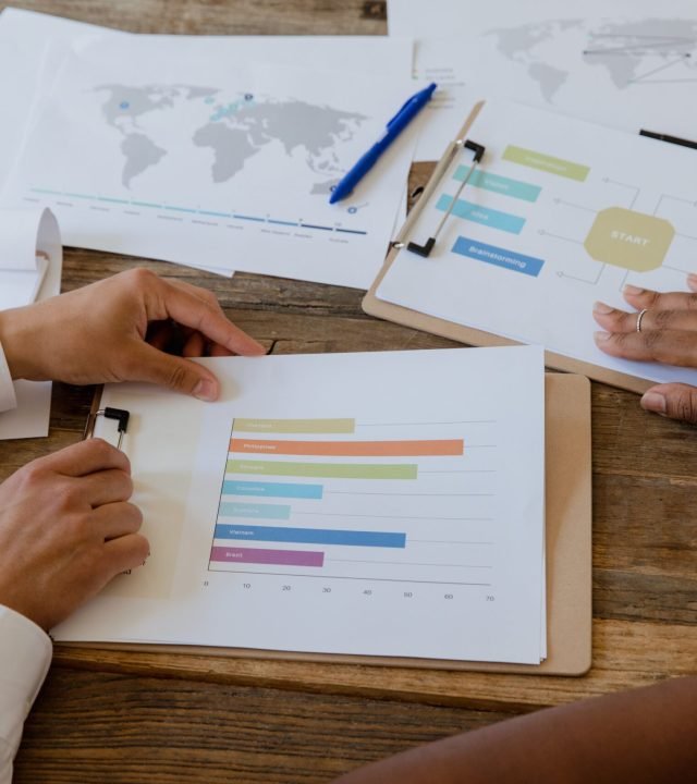 Top view of colleagues discussing charts and graphs on a wooden table during a business meeting.